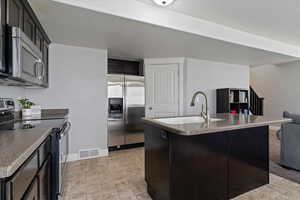 Kitchen featuring stainless steel appliances, a kitchen island with sink, a textured ceiling, open floor plan, and dark cabinetry