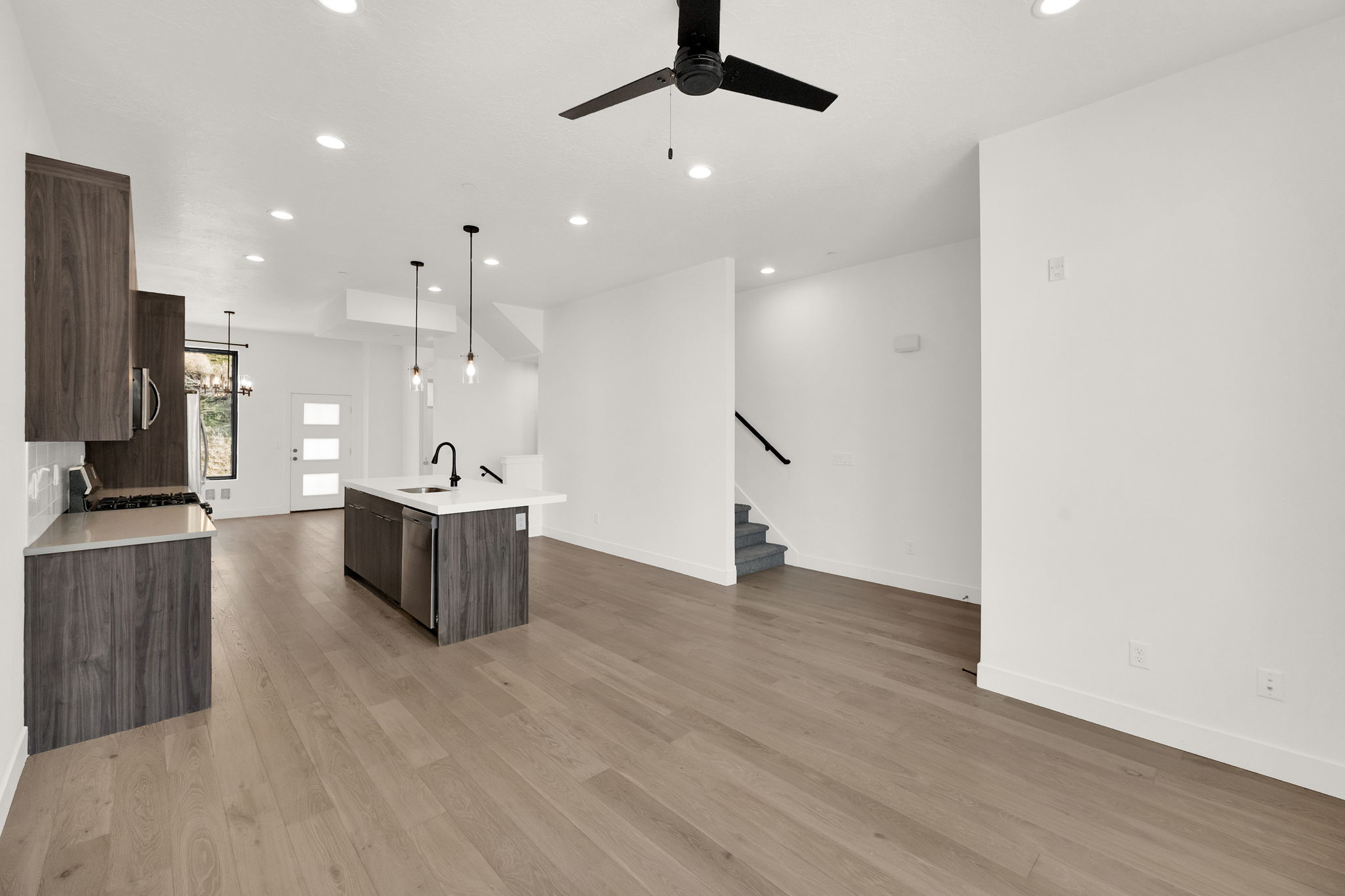 Kitchen with dark wood finish cabinetry, open floor plan, a center island with sink, a ceiling fan, and light wood-style flooring