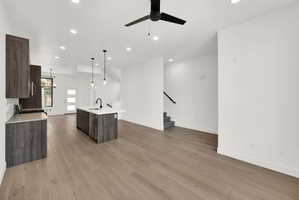 Kitchen with dark wood finish cabinetry, open floor plan, a center island with sink, a ceiling fan, and light wood-style flooring