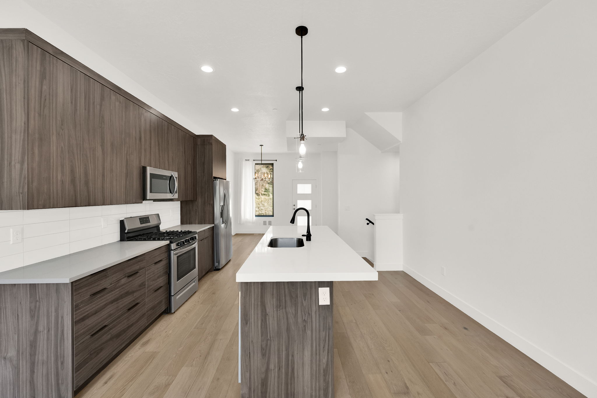 Kitchen with modern cabinets, an island with sink, stainless steel appliances, dark wood finish cabinetry, and pendant lighting