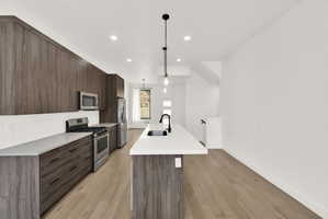 Kitchen with modern cabinets, an island with sink, stainless steel appliances, dark wood finish cabinetry, and pendant lighting