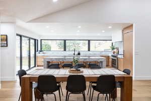 Kitchen with light wood finished floors, stainless steel stove, modern cabinets, lofted ceiling, and light wood finish cabinetry