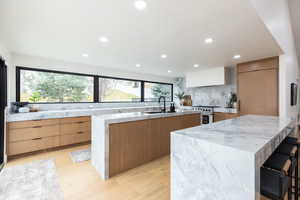 Kitchen with a kitchen breakfast bar, light stone counters, two tone cabinets, high end stainless steel range oven, and recessed lighting