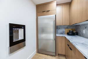 Kitchen featuring light stone counters, stainless steel built in fridge, modern cabinets, light wood finished floors, and decorative backsplash