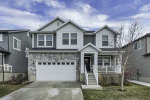 Craftsman-style home featuring an attached garage, stone siding, concrete driveway, and a front lawn