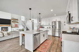 Kitchen featuring stainless steel appliances, open floor plan, hanging light fixtures, and white cabinetry