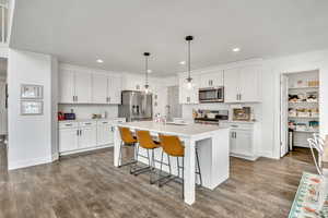 Kitchen featuring a breakfast bar, a kitchen island with sink, hanging light fixtures, and white cabinets