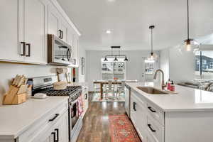 Kitchen featuring stainless steel appliances, white cabinetry, pendant lighting, dark wood-style flooring, and light stone counters