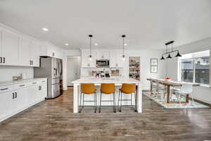 Kitchen with decorative light fixtures, stainless steel appliances, a breakfast bar area, white cabinetry, and a kitchen island with sink