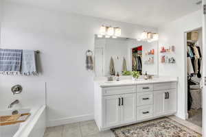 Full bathroom featuring double vanity, a garden tub, a spacious closet, and light tile patterned floors