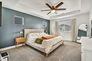 Carpeted bedroom featuring a raised ceiling and a ceiling fan