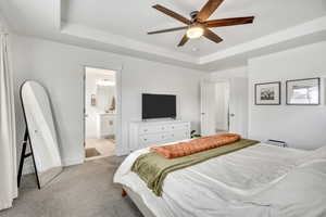 Bedroom with a raised ceiling, light colored carpet, a ceiling fan, and ensuite bathroom