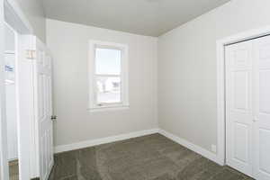 Unfurnished bedroom with dark colored carpet, a closet, and a textured ceiling