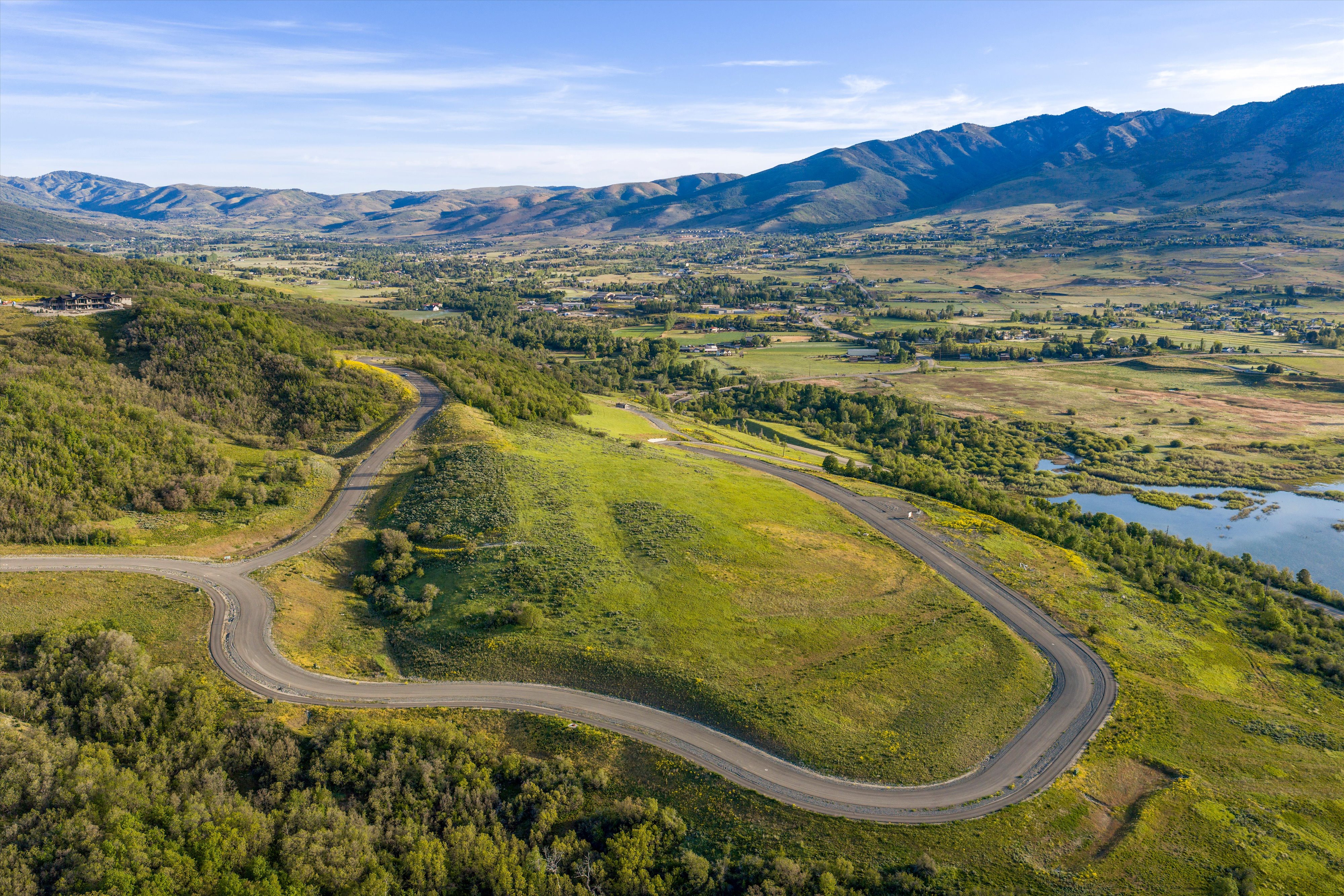 Winding paved road traversing rolling green hills, surrounded by expansive natural landscapes and distant mountains