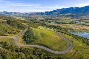 Winding paved road traversing rolling green hills, surrounded by expansive natural landscapes and distant mountains