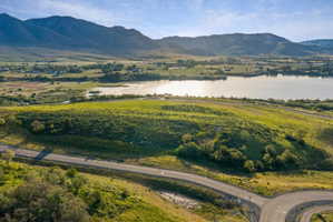 Expansive land parcel featuring a paved roadway, verdant hillsides, and distant water frontage with mountain backdrop