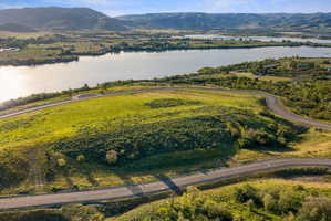 Expansive land parcel featuring paved roads, lush green and shrub vegetation, and surrounding water bodies with distant mountains