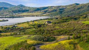 Expansive hillside property featuring a winding unpaved road, diverse natural vegetation, and distant water frontage
