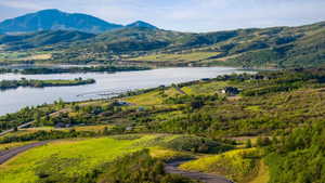 Expansive landscape featuring a large body of water, rolling green hills, distant mountains, and scattered residential properties