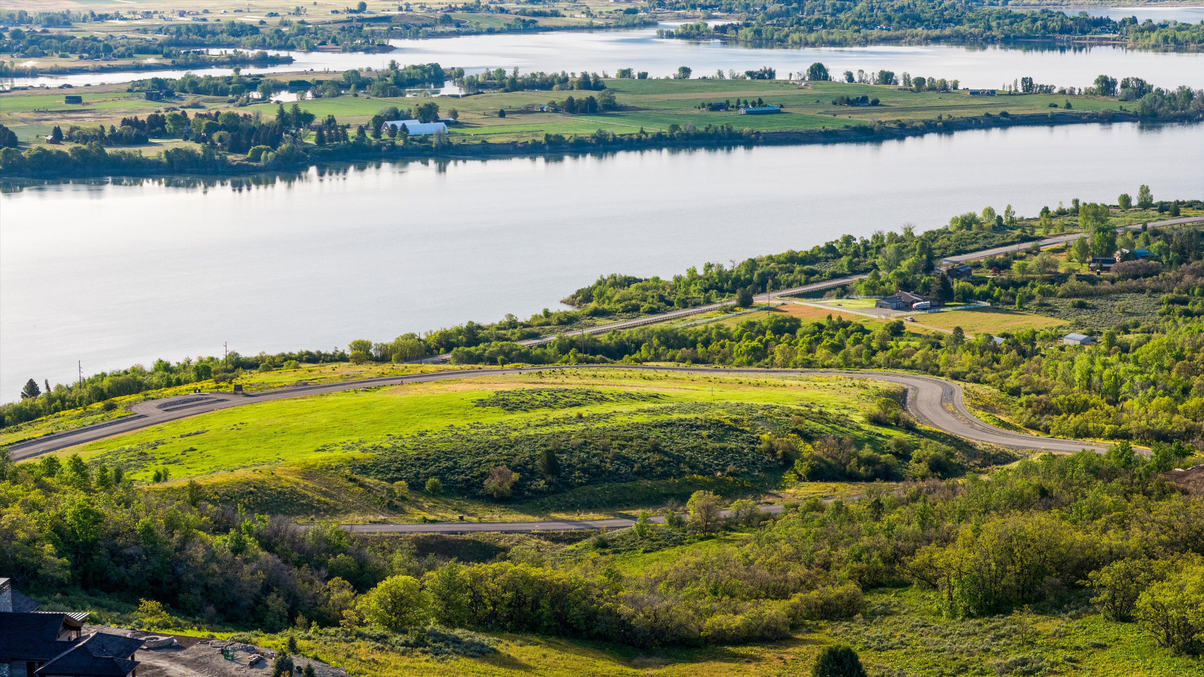 Expansive water body with verdant tree-lined shores, surrounded by agricultural fields and distant hills