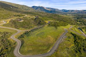 Expansive mountain landscape featuring paved winding roads, verdant hillsides, and distant peaks