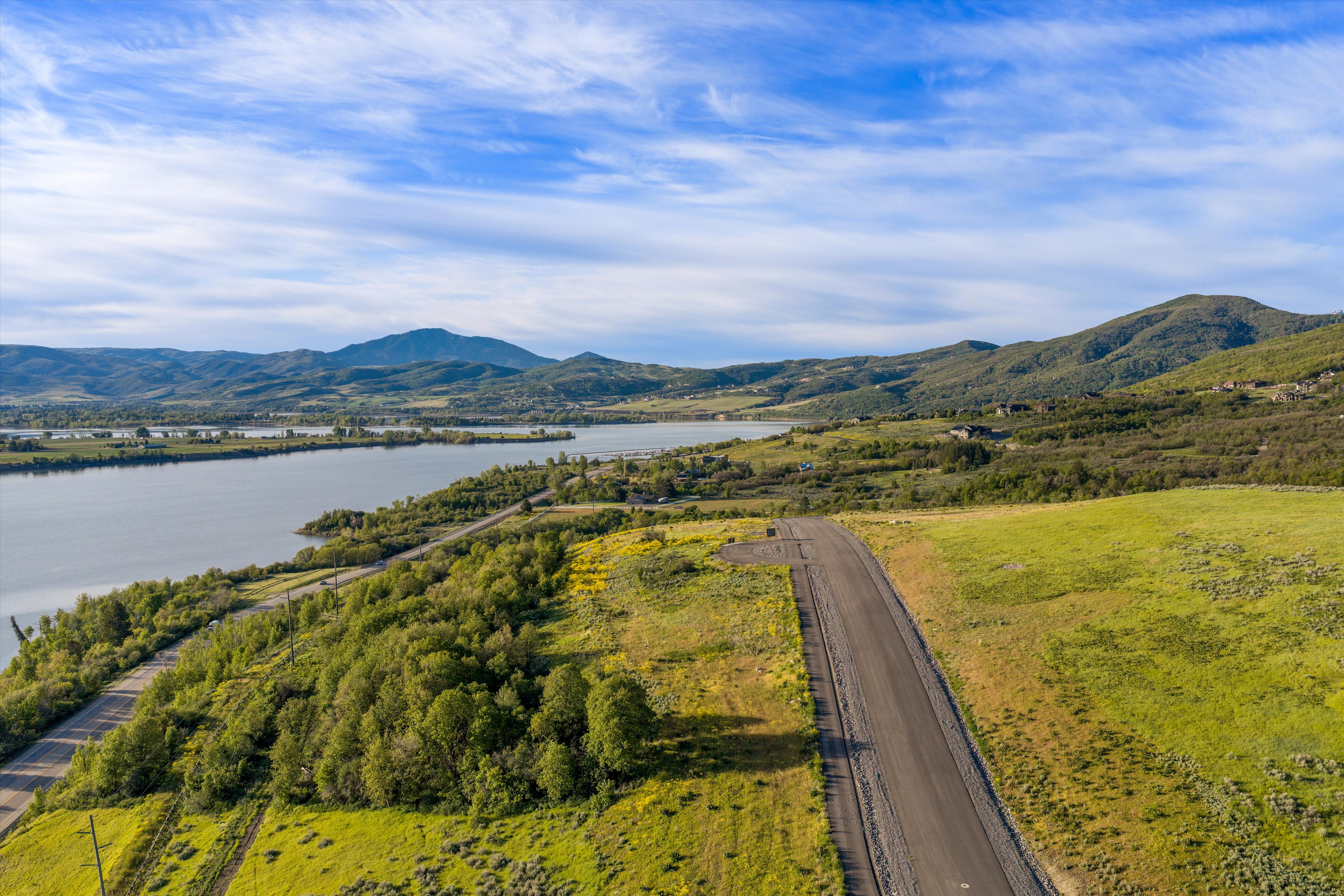 Expansive land parcel featuring a paved road, natural green landscaping, and distant water views