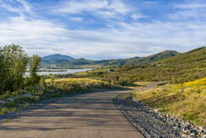 Paved road winding through a natural landscape featuring distant mountains, a body of water, and scattered residences