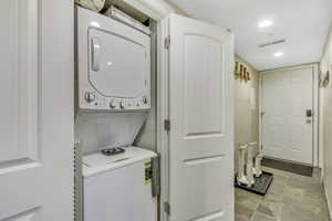 Laundry room with stacked washer / dryer, recessed lighting, and light stone finish floors