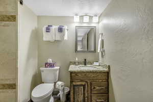 Bathroom with a textured ceiling, vanity, a textured wall, and tiled shower