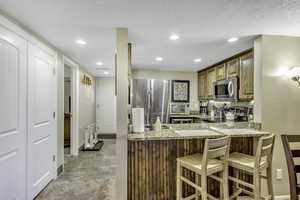 Kitchen with stainless steel appliances, light stone finish floors, light stone counters, a breakfast bar, and brown cabinets