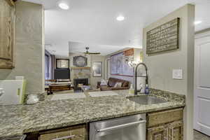 Kitchen featuring stainless steel dishwasher, a fireplace, brown cabinets, ceiling fan, and recessed lighting
