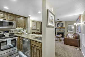 Kitchen featuring appliances with stainless steel finishes, light stone counters, a lit fireplace, light colored carpet, and brown cabinetry