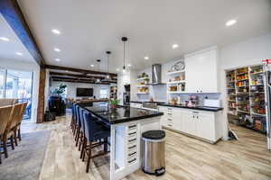 Kitchen with open shelves, white cabinetry, decorative light fixtures, a spacious island, and a kitchen bar