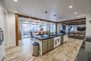 Kitchen with pendant lighting, light wood-type flooring, an island with sink, open floor plan, and beamed ceiling