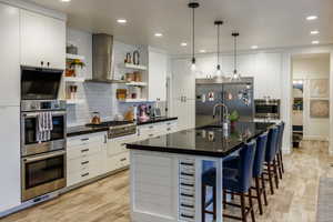 Kitchen with open shelves, built in appliances, white cabinetry, pendant lighting, and a spacious island