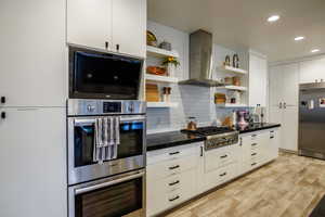 Kitchen with open shelves, exhaust hood, stainless steel appliances, recessed lighting, and white cabinets