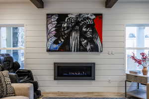 Living area featuring beamed ceiling, wood finished floors, wood walls, and a glass covered fireplace