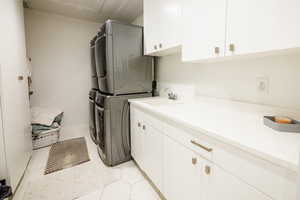 Laundry area featuring cabinet space, stacked washing machine and dryer, and light tile patterned floors