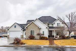View of front facade with a shingled roof, board and batten siding, concrete driveway, a garage, and stone siding