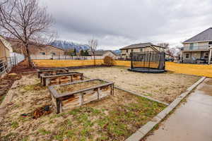 Fenced yard with a trampoline, a residential view, a vegetable garden, and a mountain view