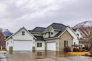 View of front of home with a mountain view, board and batten siding, roof with shingles, stone siding, and driveway