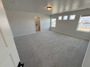 Unfurnished bedroom featuring carpet flooring, ensuite bath, and a textured ceiling