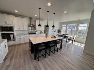 Kitchen with a breakfast bar area, oven, hanging light fixtures, built in microwave, and an island with sink