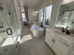 Ensuite bathroom featuring a marble finish shower, two vanities, plenty of natural light, and a soaking tub