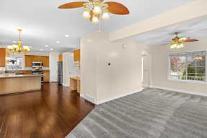Unfurnished living room featuring ceiling fan, a chandelier, arched walkways, and dark wood-style floors
