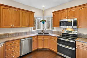 Kitchen featuring stainless steel appliances, wood finish cabinets, dark wood finished floors, and light countertops