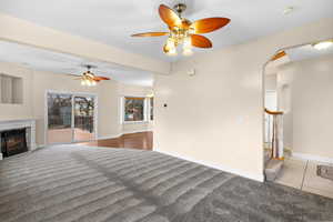 living room with a ceiling fan, a warm lit fireplace, carpet flooring, and arched walkways