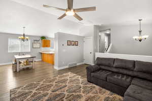 Living room featuring suspended lighting, ceiling fan, dark wood-style floors, and vaulted ceiling