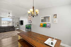 Dining room featuring ceiling fan, dark wood-style flooring, a chandelier, and lofted ceiling