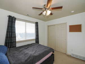Bedroom with light carpet, a textured ceiling, a ceiling fan, and a closet